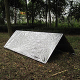 Abri de survie improvisé avec couverture réfléchissante dans une forêt