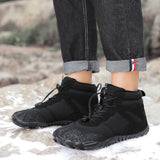 Bottes de randonnée noires imperméables pour femmes, vues de côté sur un sentier rocheux enneigé