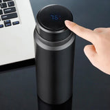 Bouteille d'eau thermique noire avec affichage de température 76°C, utilisée près d'un ordinateur portable