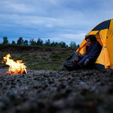 Campeur près d'une tente jaune, utilisant un sac de couchage pour se réchauffer près d'un feu de camp