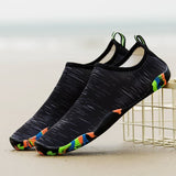 Chaussures aquatiques noires avec motifs colorés sur le bord, posées sur le sable de la plage
