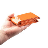 Couverture de survie orange pliée, tenue dans une main pour montrer la compacité