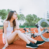 Femme assise sur une piste rouge avec un vélo, portant des chaussures de sport noires