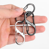 Mousquetons noirs et argentés de type S tenus dans une main, pratiques pour porte-clés et accessoires de camping