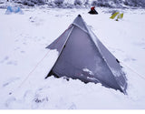 Tente de randonnée argentée installée dans la neige, vue de face avec plusieurs tentes en arrière-plan