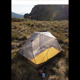 Tente de camping ultralégère montée en plein air sur un terrain rocheux avec matelas jaune à l'intérieur