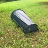 Tente de camping noire pour une personne, installée sur un sol herbeux, vue arrière