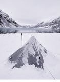 Tente de randonnée argentée pour une personne, installée dans un paysage enneigé avec vue sur le lac et montagnes