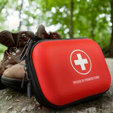 Trousse de premiers secours posée sur un sol forestier, accompagnée de bottes de randonnée, prête pour les urgences en plein air